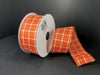 A partially unrolled spool of 1.5X10Y Dark Orange CreamStark Plaid Ribbon (61025-09-19) with a white checkered pattern is displayed against a plain black background.