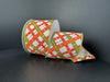 A roll of 2.5x10yd cream, orange, and moss yellow Wrigley plaid ribbon (cream canvas with orange-moss-yellow accents, item 61516-40-06) is partially unrolled on a dark surface against a dark background.
