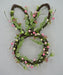 The 17 Easter Bunny Head 63764 is a whimsical wreath, ideal for Easter decor. Crafted from twigs, its adorned with pink and white eggs and green and white foliage on a plain background.