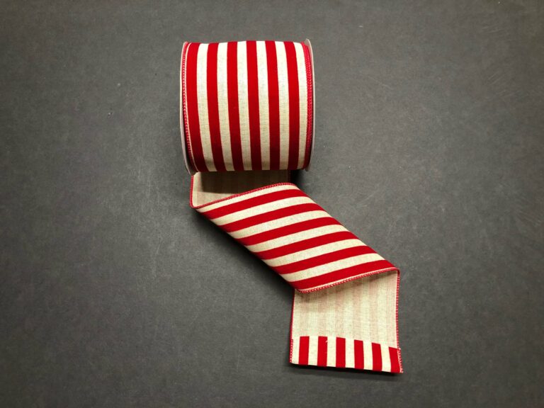 A 2.5X10Y Natural/Red Flocked Cabana Stripes Ribbon (71211-40-10) displays its bold red and natural vertical stripes and classic flocked texture, unrolled on a dark surface.
