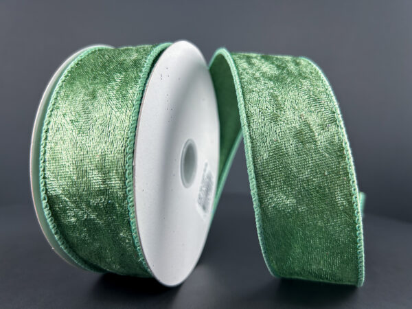 The 1.5X10Y Sage Lush Velvet Ribbon (72430-09-06) is shown with its white core against a dark gray backdrop, its shiny, textured sage material unspooled and elegantly curved to the side.