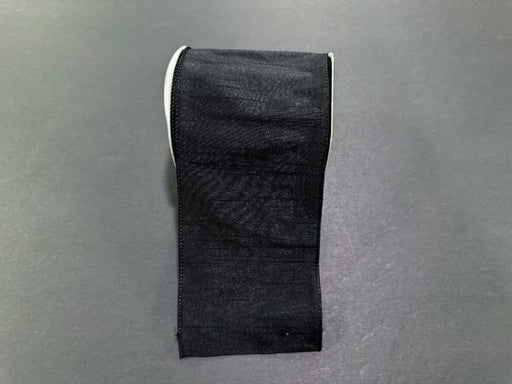A roll of 4"X10Y Black Faux Dupioni Ribbon (72434-04-21), reminiscent of a sleek black strip, sits on a gray surface.