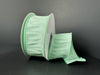 A spool of 1.5X10Y Mint Faux Dupioni Ribbon 72434-09-06 is partially unwound, showcasing its wide textured finish and decorative pleated edges against a plain dark background.