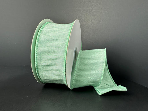 A spool of 1.5X10Y Mint Faux Dupioni Ribbon 72434-09-06 is partially unwound, showcasing its wide textured finish and decorative pleated edges against a plain dark background.