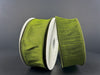 Two spools of 1.5X10Y Moss Green Faux Dupioni Ribbon 72434-09-08 lie on a dark surface, each wrapped around a gray cylindrical spool. The ribbons luxurious sheen and rich color stand out beautifully against the neutral background, showcasing their texture.