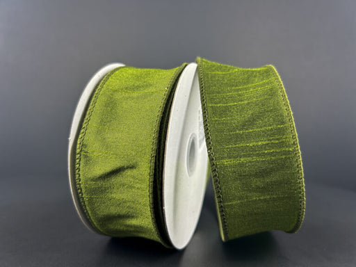 Two spools of 1.5X10Y Moss Green Faux Dupioni Ribbon 72434-09-08 lie on a dark surface, each wrapped around a gray cylindrical spool. The ribbons luxurious sheen and rich color stand out beautifully against the neutral background, showcasing their texture.