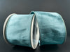 Two spools of 2.5X10Y Dusty Blue Faux Dupioni Ribbon (72434-40-05) sit against a dark background, showcasing their subtle sheen and soft texture.