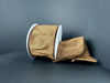 A spool of 2.5X10Y Brown Faux Dupioni Ribbon (72434-40-38), featuring white edges, is partially unrolled and displayed on a dark, curved surface with a plain dark background.