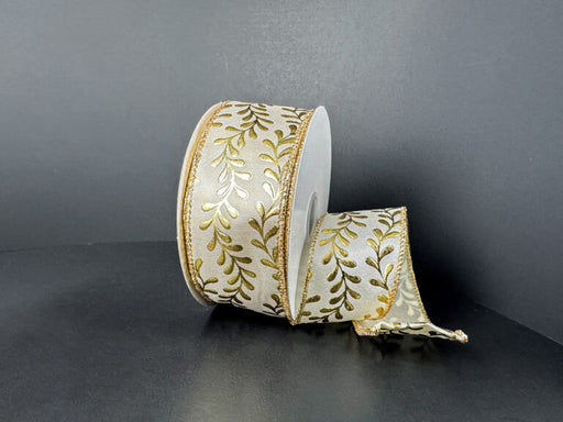 A spool of 1.5X10Y Ivory Satin/Gold Embossed Vines Ribbon (73528-09-41) with a gold leaf pattern and gold edges rests against a dark background, partially unrolled and elegantly draping to the side.