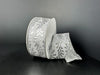 A roll of 1.5X10Y White Satin/Silver Embossed Vines Ribbon (73528-09-42) is shown against a dark background, with a portion unrolled and gracefully draped to highlight its elegant silver vine pattern.