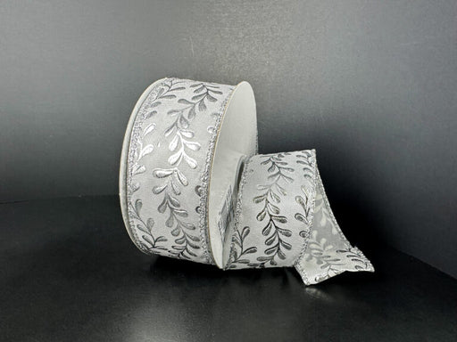 A roll of 1.5X10Y White Satin/Silver Embossed Vines Ribbon (73528-09-42) is shown against a dark background, with a portion unrolled and gracefully draped to highlight its elegant silver vine pattern.
