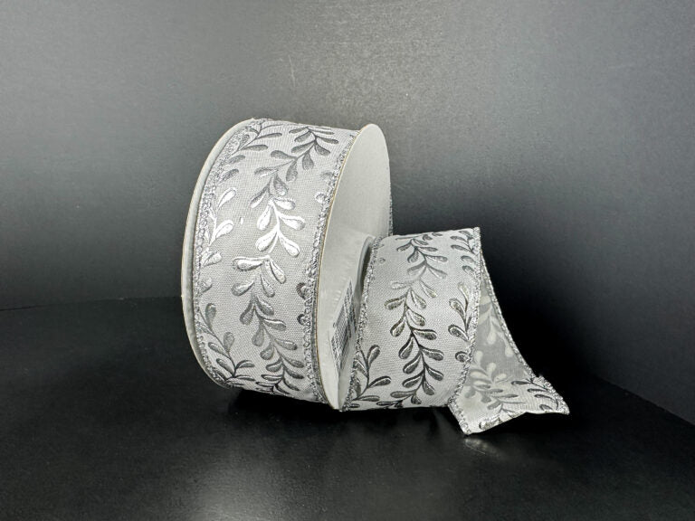 A roll of 1.5X10Y White Satin/Silver Embossed Vines Ribbon (73528-09-42) is shown against a dark background, with a portion unrolled and gracefully draped to highlight its elegant silver vine pattern.