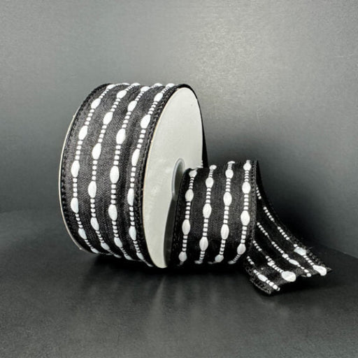 A spool of 1.5X10Y Black/White Snowball Weave Ribbon (73539-09-21), featuring stitched oval shapes and lines in a black and white design on a plain dark background.