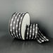 A spool of 1.5X10Y Black/White Snowball Weave Ribbon (73539-09-21), featuring stitched oval shapes and lines in a black and white design on a plain dark background.