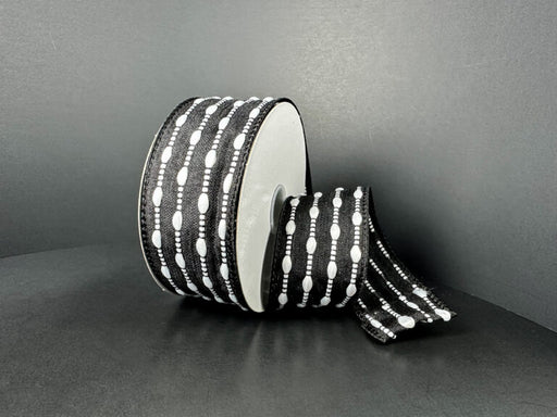 A spool of 1.5X10Y Black/White Snowball Weave Ribbon (73539-09-21), featuring stitched oval shapes and lines in a black and white design on a plain dark background.