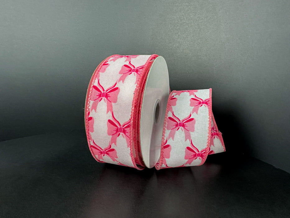 A spool of 1.5X10Y White Ponche Satin/Pink Bows Ribbon 73543-09-03 features pink bows on white satin, with one end unrolled and curved beside the spool, set against a plain dark background.
