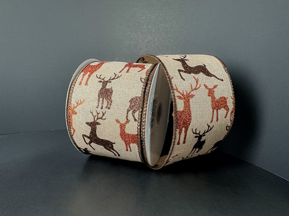 Two rolls of 2.5X10Y Natural Linen/Brown-Rust Glitter Deer Ribbon (73552-40-31) with repeating deer silhouettes in brown, black, and red on natural linen, set against a dark background.