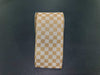 A roll of 4X10Y Cream Canvas/Gold Paint Chex Ribbon (73553-04-15) is standing upright on a dark, smooth surface.