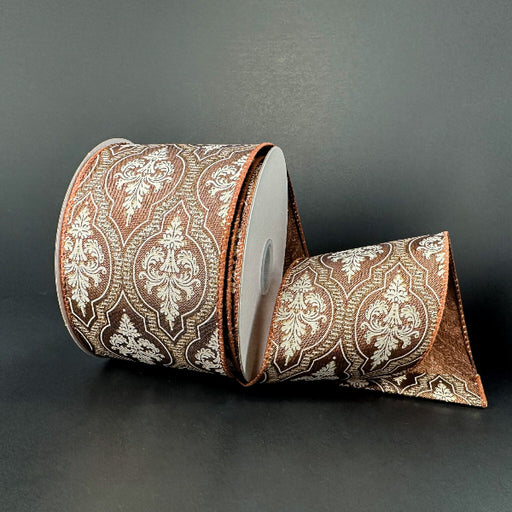 A 2.5x10Y Brown Satin/Demask Quatrefoil Ribbon (73556-40-38) with a white and gold ornate pattern is displayed on a dark surface, partially unrolled and elegantly draped in front.