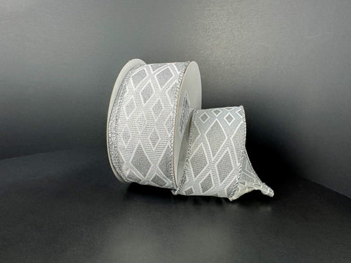 A spool of 1.5X10Y White-Silver Linen/Silver Metallic Diamond Cascade Ribbon (73559-09-16) with a geometric silver diamond pattern is unwound on a dark, plain surface and background.