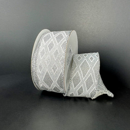 A spool of 1.5X10Y White-Silver Linen/Silver Metallic Diamond Cascade Ribbon (73559-09-16) with a geometric silver diamond pattern is unwound on a dark, plain surface and background.