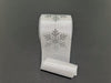 A 4X10Y White Ribbed Satin/Silver Giant Glitter Snowflake Ribbon (73569-04-16) with shimmering snowflake designs lies on a plain dark background.