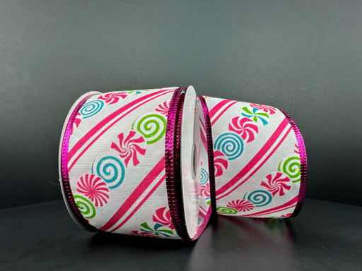 Two spools of the 2.5X10Y White Linen/Christmas Candy-Fuchsia-White Diagonal Stripe-Fuchsia Metallic Edge Ribbon 76307-40-44 stand against a dark background, featuring pink, blue, and green swirl candies on white with shiny metallic pink edges.