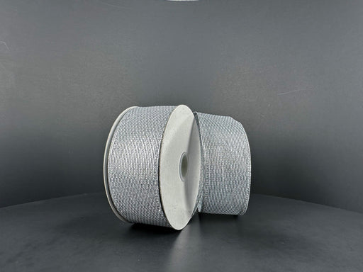 Two spools of 1.5X10Y Silver Stairstep Woven Metallic Ribbon (76310-09-51) sit side by side on a dark, matte surface against a neutral background.