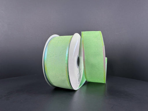Two rolls of 1.5"X10Y Lt Green Metallic Satin/Lt Green Metallic Edge ribbon stand vertically against a dark background. One roll displays more ribbon, while the other shows less. The ribbons have a subtle sheen and appear to be made of fabric material.