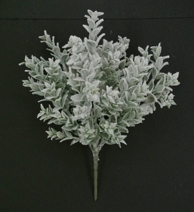The 18" Snowed Tea Leaf Bush with 7 Stems (85286) features elegant white foliage that stands out beautifully against dark surfaces, creating a striking display of delicate charm.