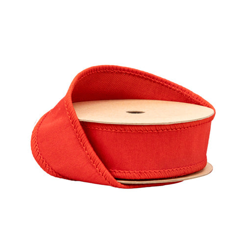 A spool of 1″ Red Wired Dupioni Ribbon with Metallic Fuse Backing (10 yards, 91224-250-25E), partially unrolled and curled around its cardboard reel, is shown against a white background—perfect for Christmas decorating.