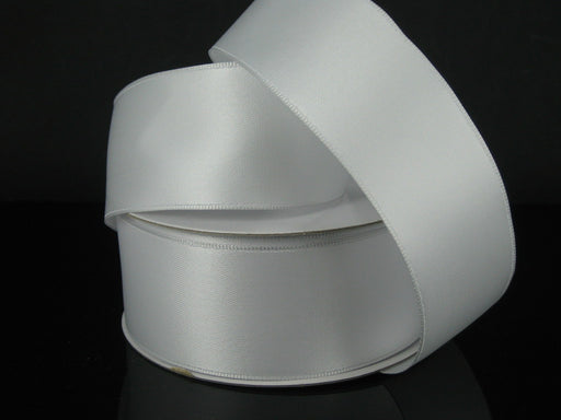 The 1.5 by 25 Yards White Wired Double Faced Satin Ribbon 950109-01 glistens subtly as it unwinds from its coil on a black surface, offering a smooth texture perfect for any sophisticated project or decor.