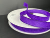 The 7/8X50Y (42466-05-11C) Purple Flower Embossed Ribbon, partially unwound, is displayed on a dark background and elegantly wound around a white circular base.