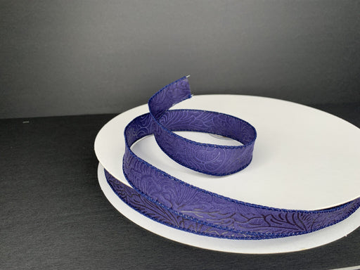 A roll of 7/8X50Y Navy Flower Embossed Ribbon 984205-27C is partially unrolled on a white spool against a dark background, showcasing its delicate, intricate floral pattern.