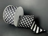 A 2.5 x 10 yd double-sided ribbon spool (D73582-40-20) in black satin with large white dots on one side and black-white glitter candy cane stripes on the other is partially unrolled against a plain black background.