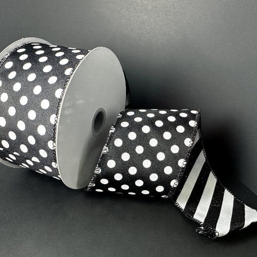 A 2.5 x 10 yd double-sided ribbon spool (D73582-40-20) in black satin with large white dots on one side and black-white glitter candy cane stripes on the other is partially unrolled against a plain black background.