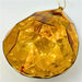 A 6.3" x 4" x 9" Amber Plastic Drop Ornament (DCORN5408AM) with a faceted, geometric design hangs from a thin gold string, reflecting light against a plain white background.