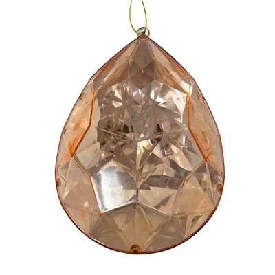 A 6.3" x 4" x 9" Rose Gold Plastic Drop Ornament (DCORN5408RS) with geometric facets and a teardrop shape hangs from a thin string, beautifully reflecting light with its subtle rose gold tint.