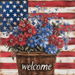 The 10 x 10 Patriotic Welcome Basket Sign TTE-257 features welcome elegantly on a metal sign, filled with vibrant red, white, and blue flowers. An American flag backdrop proudly displays its stars and stripes.