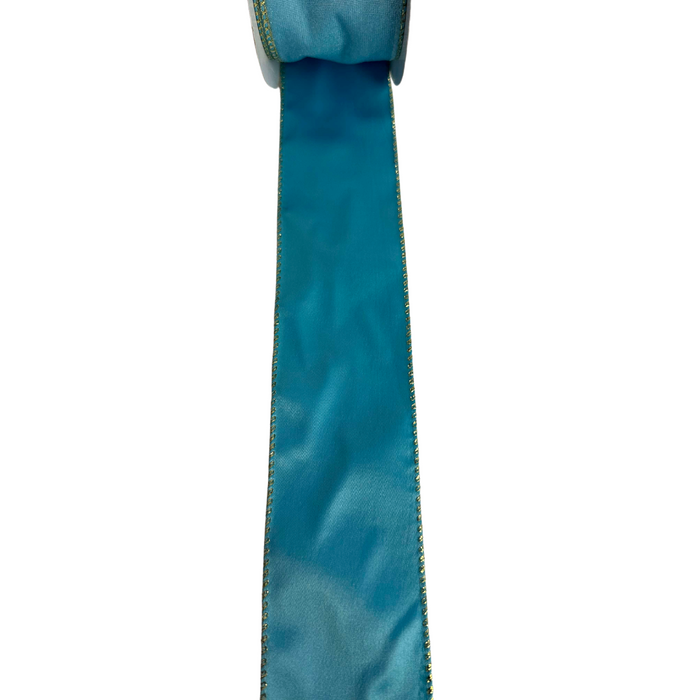 A spool of 2.5 light blue velvet ribbon with a satin back unrolls on a white background, its luxurious texture and vibrant gold edges beautifully contrasting against the plain scene.