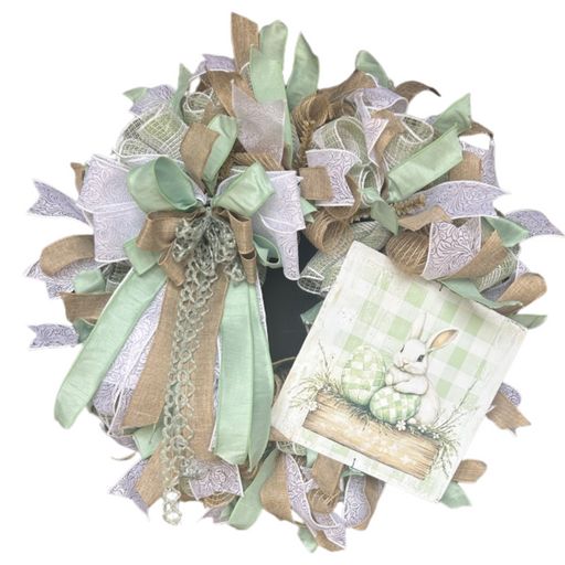 The Sage Easter Bunny Completed Wreath features green, white, and burlap ribbons, a large bow, and a sign with a white bunny and green Easter eggs on plaid. Shipping is included for your convenience!.