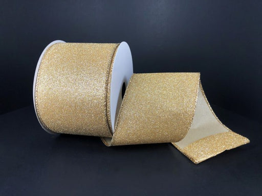 The 2.5X10Y Champagne All Flat Glitter Ribbon X820640-14, with a white spool, rests on a dark surface. The sparkling champagne ribbon is partially unrolled, revealing its textured glitter finish.