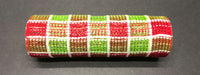 A 10"X10Y roll of Red-Lime Fuzz Snow Chex XB105810-09, featuring a woven pattern in red, green, white, and brown with a shiny texture and colors arranged in a repeating sequence, sits on a dark surface.