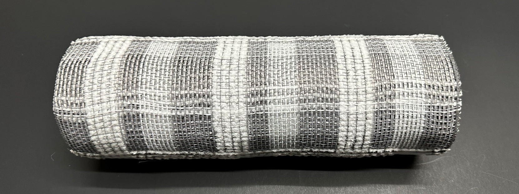 A roll of 10" Gray & White Fuzzy Plaid Mesh (XB235810-51) rests on a dark, smooth surface.