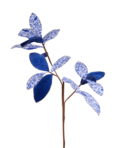 A branch adorned with blue and white patterned leaves, some with intricate florals and others solid blue, mirrors the elegance of the 27 Glitter Velvet Magnolia Leaf Spray XS253103 against a crisp white backdrop.