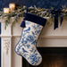 Flat metal Christmas sign printed with a blue-and-white chinoiserie stocking featuring birds, flowers, navy velvet trim, and a decorated mantel