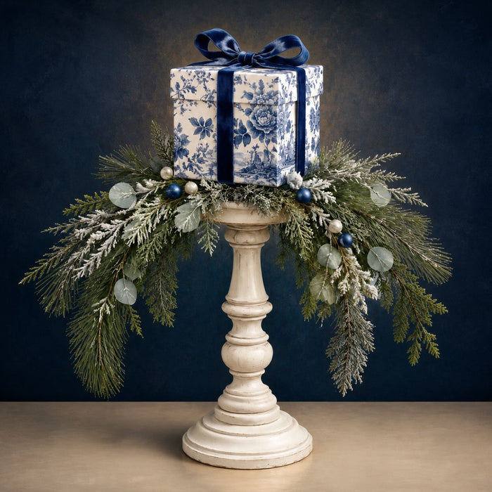 Blue and white chinoiserie Christmas gift box with navy velvet bow, frosted greenery, and eucalyptus arranged on a white candlestick