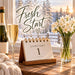 Flat metal sign featuring Fresh Start lettering, January 1 calendar, champagne bottle and flute, white winter flowers in a glass vase, and snow-covered trees outside a sunlit window. TTE-851.