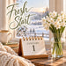 Flat metal sign featuring Fresh Start lettering, January 1 desk calendar, cream-colored coffee mug on stacked books, white narcissus flowers in a glass vase, cozy knitted blanket, and snowy winter scenery outside a window. TTE-852.