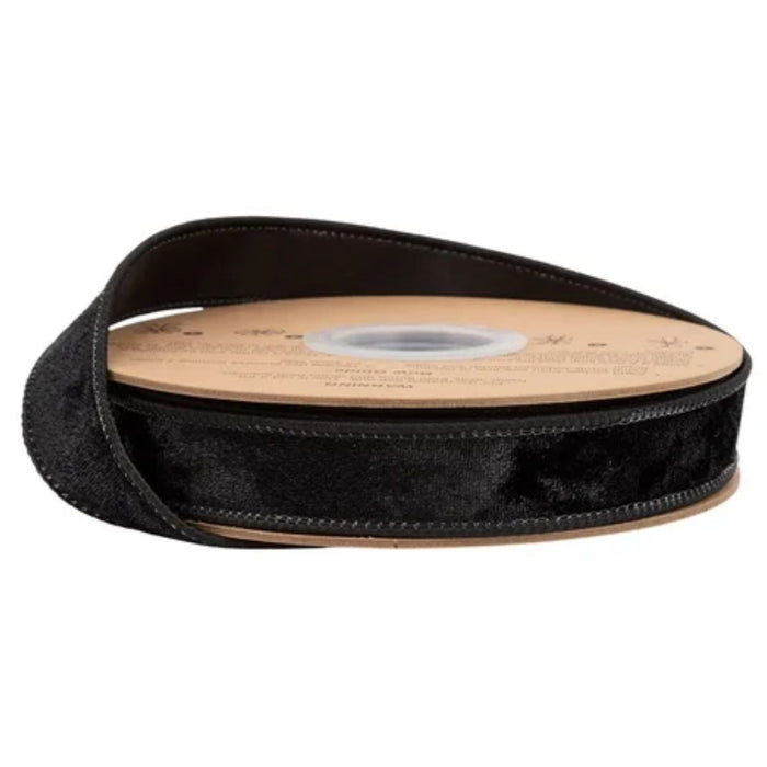 A spool of Heritage Black Velvet with Black Back Wired Ribbon 1 Inch x 10 Yards (7005W-030-25E), featuring a cardboard center and partially unrolled against a white background, makes an elegant decorating ribbon for your holiday crafts.